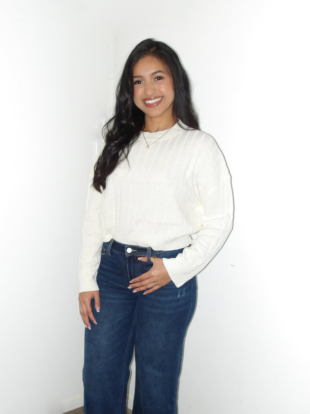 Woman wearing a white blouse and blue jeans against a white wall.